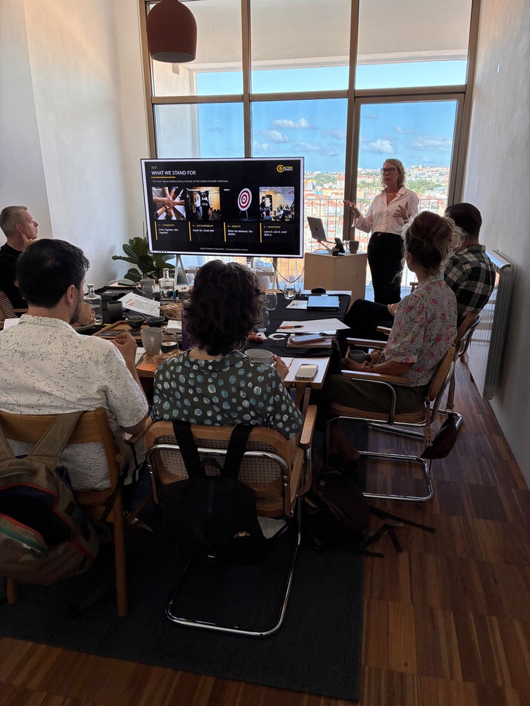 Jessica leading a Lisbon Growth Collective session — the group gathered around the table while a session slide is presented
